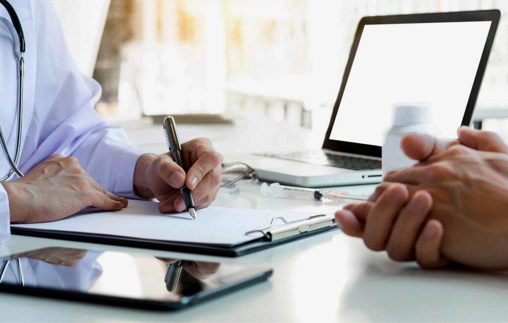 close up of dr and patient hands at a desk, doctor is writing